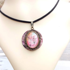 Peut inclure: Un collier ras de cou noir avec un pendentif ovale en bronze représentant une illustration aquarelle d'un vélo avec des fleurs roses et orange. Le pendentif est orné d'une bordure en filigrane décorative.