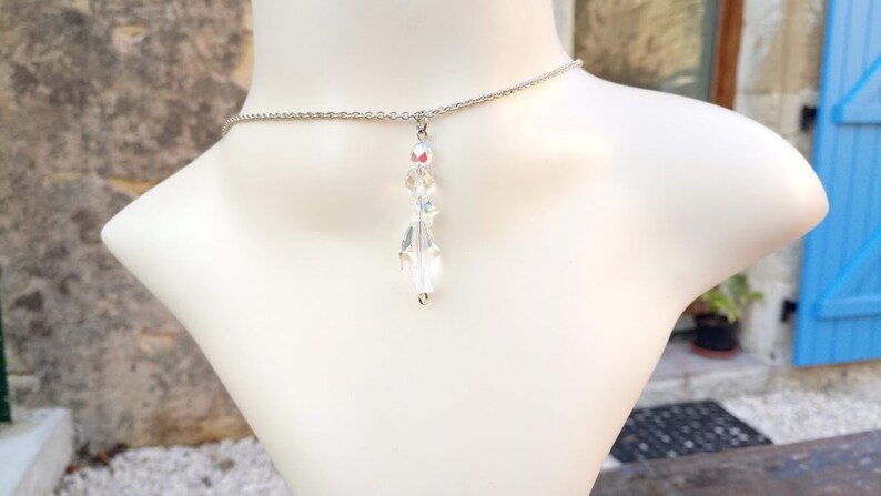 May include: A silver chain necklace with a clear crystal pendant. The pendant is made of faceted crystals that reflect light.