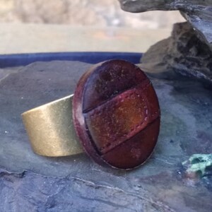 Op de afbeelding: Een bruine leren ring met een gouden band. Het leer is getextureerd en heeft een roodbruine tint.