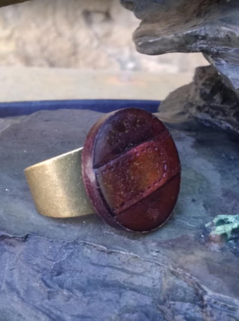 Op de afbeelding: Een bruine leren ring met een gouden band. Het leer is getextureerd en heeft een roodbruine tint.
