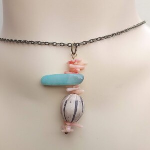 Peut inclure: Un collier d&eacute;licat avec un pendentif compos&eacute; d'une pierre bleu clair, d'une perle blanche et grise et de morceaux de corail rose.
