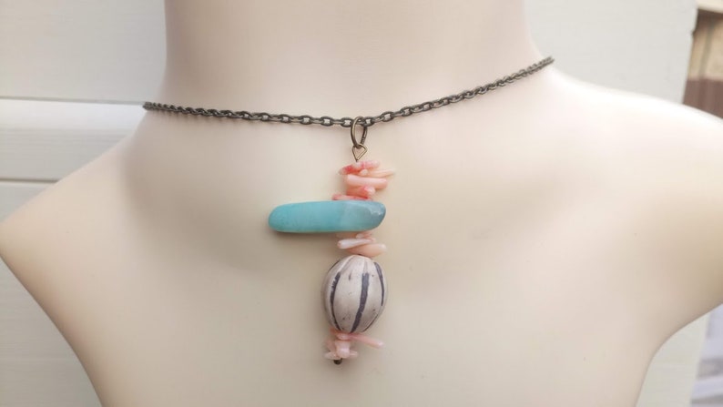 Peut inclure: Un collier d&eacute;licat avec un pendentif compos&eacute; d'une pierre bleu clair, d'une perle blanche et grise et de morceaux de corail rose.