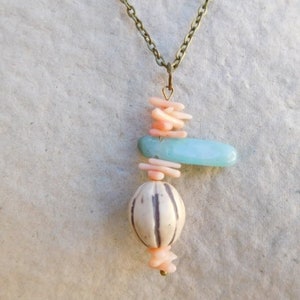 Peut inclure: Un collier d&eacute;licat avec un pendentif compos&eacute; de perles roses et bleues superpos&eacute;es. Le pendentif est suspendu &agrave; une cha&icirc;ne en laiton.