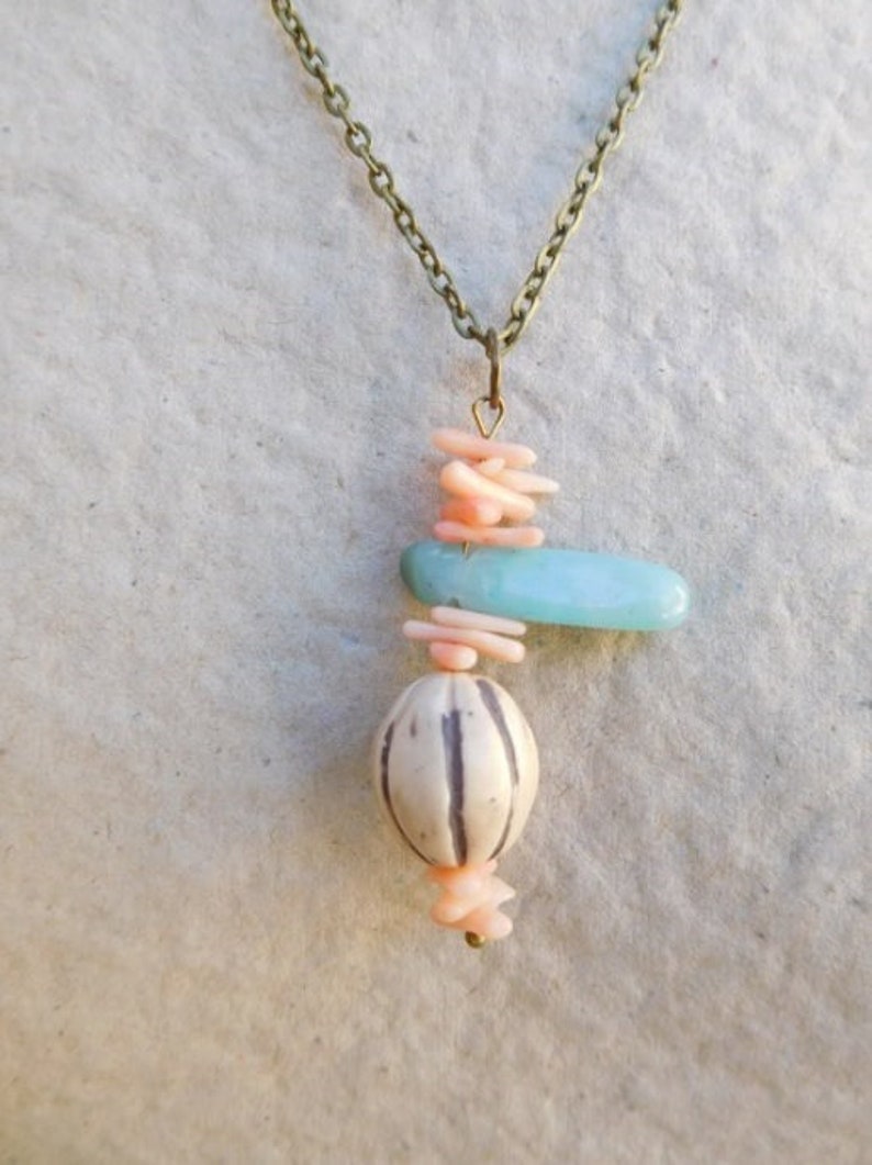 Peut inclure: Un collier d&eacute;licat avec un pendentif compos&eacute; de perles roses et bleues superpos&eacute;es. Le pendentif est suspendu &agrave; une cha&icirc;ne en laiton.