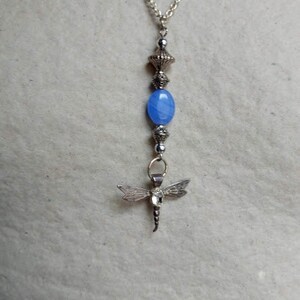 Puede incluir: Un collar de cadena de plata con una cuenta de &aacute;gata azul y un colgante de lib&eacute;lula.