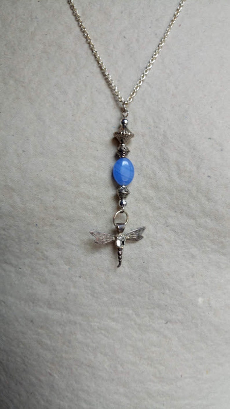 Puede incluir: Un collar de cadena de plata con una cuenta de &aacute;gata azul y un colgante de lib&eacute;lula.