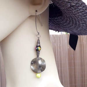 Puede incluir: Pendientes de plata con un disco redondo grande, una pequeña perla amarilla y una perla con estampado en blanco y negro.