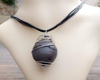 May include: A black leather cord necklace with a gray stone pendant encased in a silver wire cage.