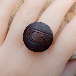 Op de afbeelding: Een bruine leren ring met een gestikt detail. De ring is rond en heeft een donkerbruine kleur.