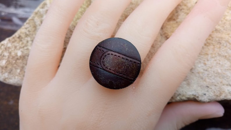 Op de afbeelding: Een bruine leren ring met een gestikt detail. De ring is rond en heeft een donkerbruine kleur.