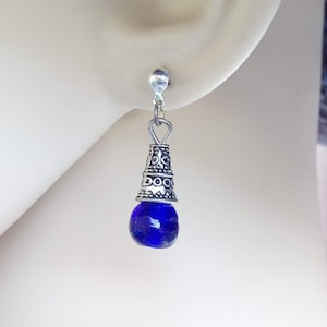 Può includere: Orecchini pendenti in argento con una perla di vetro blu e un ciondolo a forma di cono in argento con disegni intricati.
