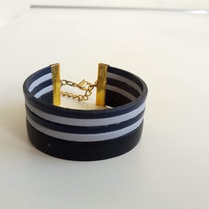 May include: A black and white striped silicone bracelet with a gold chain and clasp.