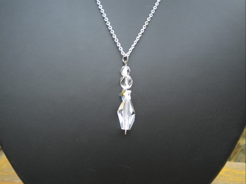 May include: A silver chain necklace with a clear crystal pendant. The pendant is made up of several faceted crystals, including a star-shaped crystal.
