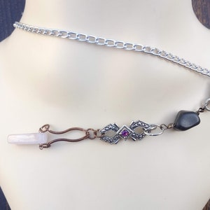 Op de afbeelding: Een zilveren ketting met een zilveren sluiting en een hanger met een zwarte steen, een roze steen en een zilveren filigraanontwerp.