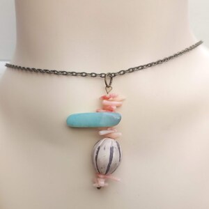 Peut inclure: Un collier d&eacute;licat en cha&icirc;ne argent&eacute;e avec un pendentif compos&eacute; d'une pierre bleu clair, d'une perle &agrave; motif blanc et noir et de morceaux de corail rose.