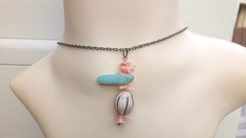 Peut inclure: Un collier d&eacute;licat en cha&icirc;ne argent&eacute;e avec un pendentif compos&eacute; d'une pierre bleu clair, d'une perle &agrave; motif blanc et noir et de morceaux de corail rose.