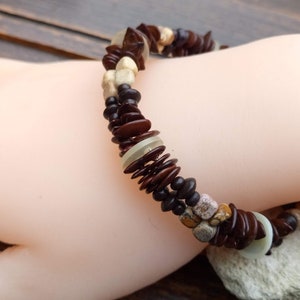 May include: A brown, white and beige beaded bracelet with a variety of shapes and sizes. The bracelet is made of natural materials and has a rustic, bohemian style.
