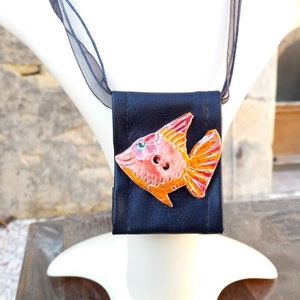 Pu&ograve; includere: Una collana in pelle nera con un ciondolo in ceramica a forma di pesce arancione e rosa. Il pesce ha un bottone per l'occhio.
