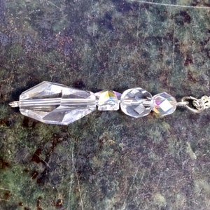 May include: A silver chain necklace with a crystal pendant. The pendant is made of faceted clear crystals and has a teardrop shape.