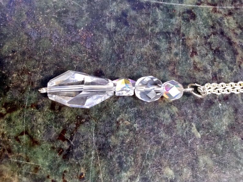 May include: A silver chain necklace with a crystal pendant. The pendant is made of faceted clear crystals and has a teardrop shape.