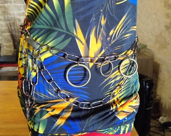 May include: A silver chain belt with multiple large rings. The belt is worn over a black and blue patterned shirt with yellow and orange accents.