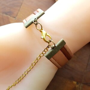 May include: A brown leather bracelet with a gold chain and a metal clasp. The bracelet is adjustable and has a layered design.