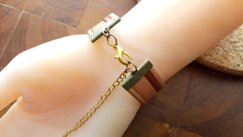 May include: A brown leather bracelet with a gold chain and a metal clasp. The bracelet is adjustable and has a layered design.