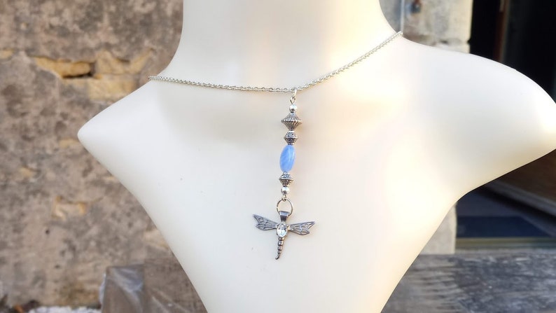 Puede incluir: Un collar de cadena de plata con un colgante de lib&eacute;lula y cuentas de vidrio azul.