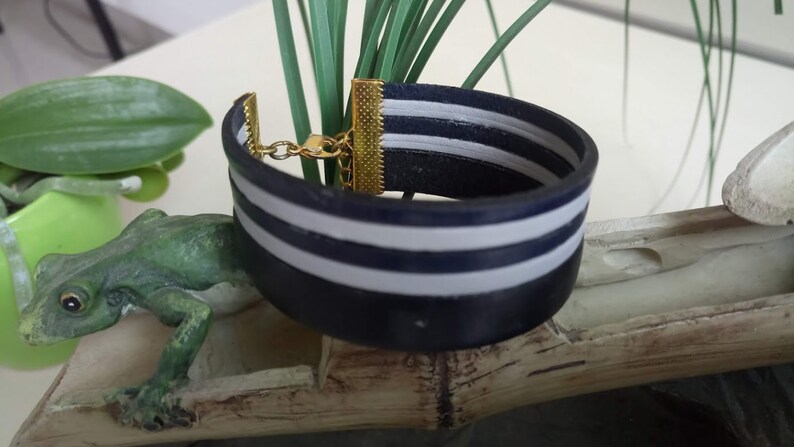 May include: A navy blue leather bracelet with two white stripes. The bracelet has a gold clasp.