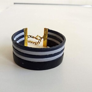 May include: A black leather bracelet with two white stripes and a gold chain closure.