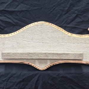 May include: A wooden wall shelf with a light gray center section and a small shelf. The ends have a curved design with a brown border and a dark brown bird footprint. The shelf is made of wood.