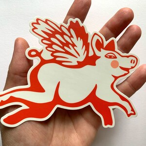 May include: A red and white sticker of a pig with wings. The pig is flying and has a happy expression on its face.