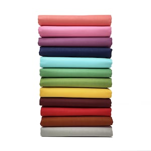 May include: A pile of folded fabric in a range of colours: coral, pink, purple, navy, teal, green, yellow, burgundy, red, brown, and grey. The fabric is stacked neatly against a white background.