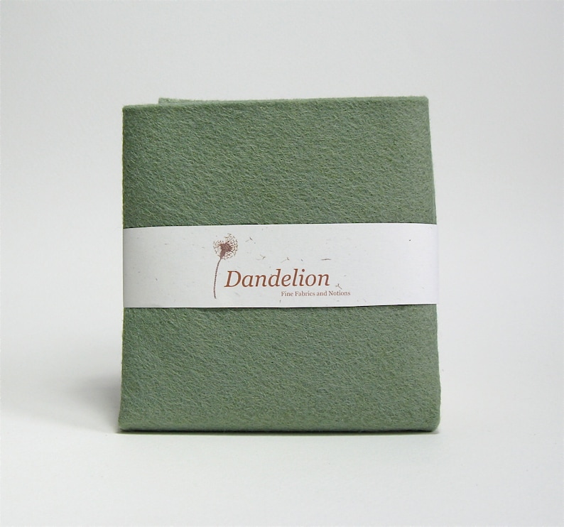 May include: A sage green felt fabric swatch with a white label that reads "Dandelion Fine Fabrics and Notions".