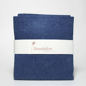 Può includere: Un foglio di tessuto in feltro blu con il testo "Dandelion Fine Fabrics and Buttons" stampato su un'etichetta bianca.