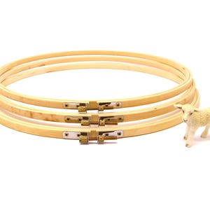 May include: Three wooden embroidery hoops stacked on top of each other. The hoops are made of natural wood and have a brass screw closure.