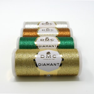 May include: Five spools of DMC Diamant metallic embroidery thread. The spools are arranged in a row from left to right: gold, green, copper, silver, and white.