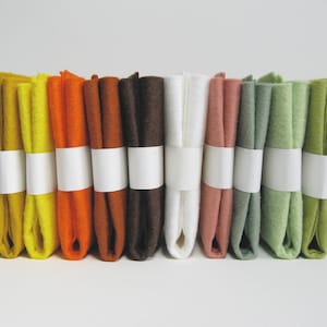 May include: A set of ten 12x18 inch felt squares in various colors, including yellow, orange, brown, white, pink, and green. The felt squares are stacked on top of each other and are wrapped with white ribbon.