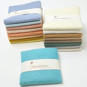 May include: A selection of felt squares in pastel shades, such as blue, pink, orange, and yellow. Each stack is bound with a white band printed with "Dandelion". The felt has a soft appearance, ideal for crafting projects.