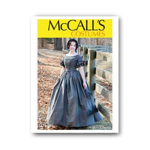 May include: McCall's Costumes pattern for a long, black and green plaid dress with a ruffled neckline and sleeves. The dress is shown on a model standing in front of a wooden fence. The pattern number is 7380 and the text "Angela Clayton" is printed below the model.