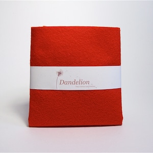 May include: A bright red felt fabric sheet with a white label that reads "Dandelion Fine Fabrics and Notions".