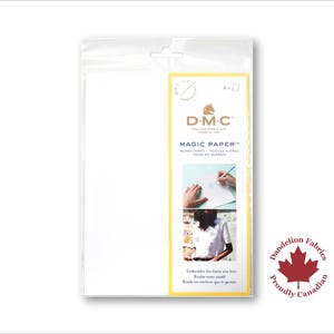 May include: A pack of DMC Magic Paper for embroidery. The pack is white with a yellow border and shows a drawing of a hand using the paper. The text on the pack reads "DMC Magic Paper" and "Black Sheet - Feuille Noire - Hoja en Blanco". The bottom of the pack features a red maple leaf with the text "Dandelion Fabrics Proudly Canadian".