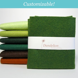 May include: A stack of felt fabric squares in various shades of green, brown, and orange. The felt is arranged in a gradient from light green to dark green. The felt is labelled "Dandelion Felt Fabrics and Notions".