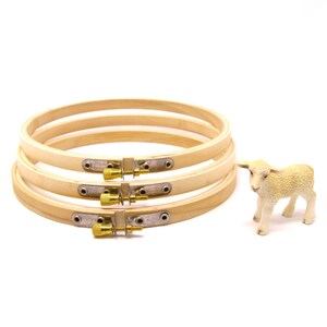 Può includere: Quattro telai da ricamo in legno chiaro con chiusure in ottone, impilati. Accanto, una piccola statuina di agnello bianco. Ideali per ricamo e lavori di cucito.