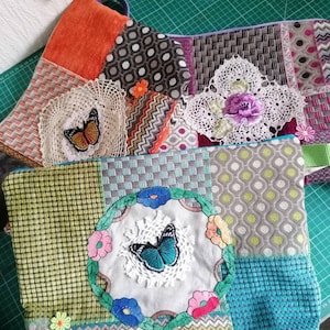 May include: Two colorful patchwork fabric pouches with butterfly embroidery. The pouch on the left has a green, blue, and white patchwork design with a blue butterfly in the center. The pouch on the right has a brown, orange, and white patchwork design with a brown butterfly in the center.