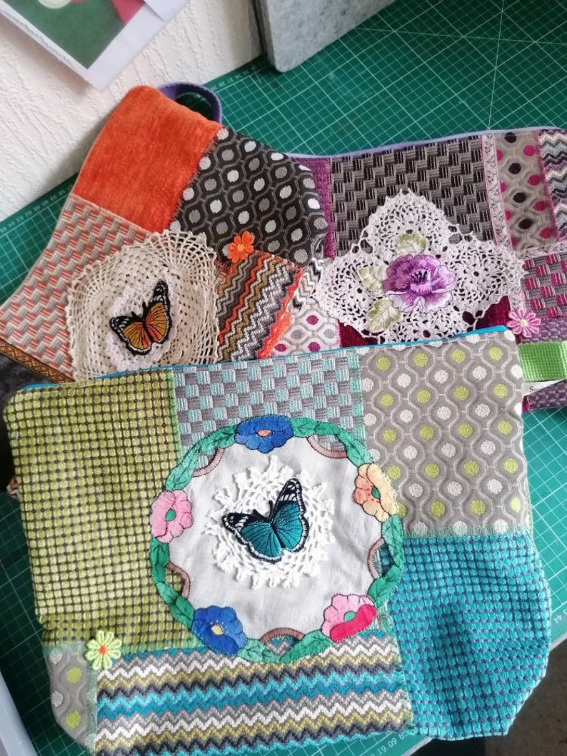 May include: Two colorful patchwork fabric pouches with butterfly embroidery. The pouch on the left has a green, blue, and white patchwork design with a blue butterfly in the center. The pouch on the right has a brown, orange, and white patchwork design with a brown butterfly in the center.
