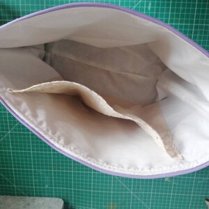 May include: A white zippered pouch with a lavender zipper and two interior pockets. The pouch is open and the interior is visible.