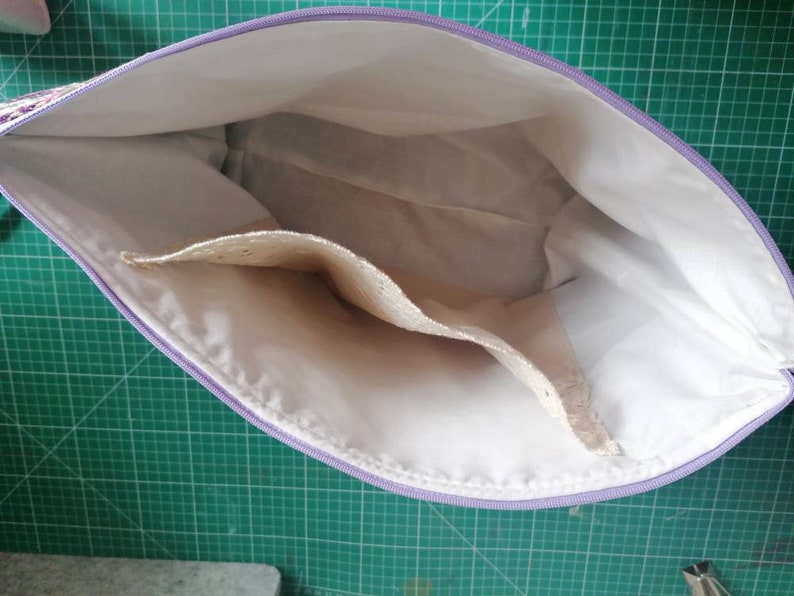 May include: A white zippered pouch with a lavender zipper and two interior pockets. The pouch is open and the interior is visible.