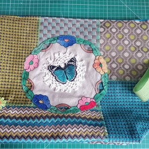 May include: A green, blue, and gray patchwork tote bag with a floral and butterfly design. The bag has a green strap with the text "SustainQuakers" on it.