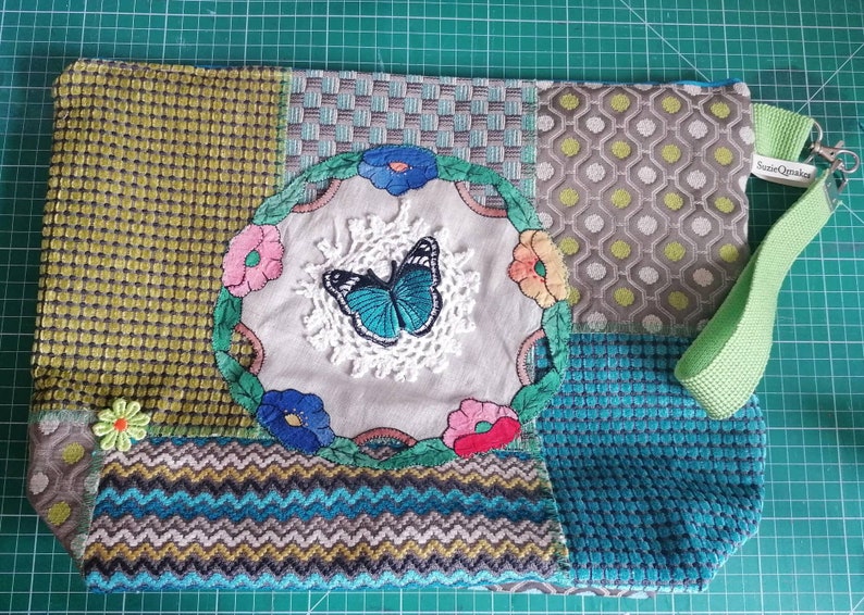 May include: A green, blue, and gray patchwork tote bag with a floral and butterfly design. The bag has a green strap with the text "SustainQuakers" on it.